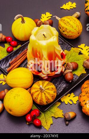 Herbstkomposition für Thanksgiving oder Halloween. Brennende geschnitzte Kerze, reife Kürbisse, Eicheln, Herbstblätter und Hagebutten. Steinbeton hintergr Stockfoto