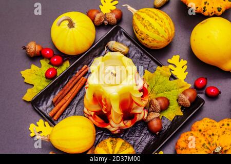 Herbstkomposition für Thanksgiving oder Halloween. Brennende geschnitzte Kerze, reife Kürbisse, Eicheln, Herbstblätter und Hagebutten. Steinbeton hintergr Stockfoto