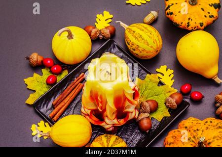 Herbstkomposition für Thanksgiving oder Halloween. Brennende geschnitzte Kerze, reife Kürbisse, Eicheln, Herbstblätter und Hagebutten. Steinbeton hintergr Stockfoto
