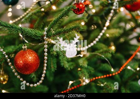 Ein Holzspielzeug in Form eines Hirschkopfes auf den Zweigen eines Weihnachtsbaums, umgeben von Perlen, Girlanden und Kugeln. Stockfoto
