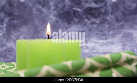 Komposition mit einer grünen Kerze auf einem Tisch mit einer grünen Leinenserviette vor einem schönen grauen Marmorboden. Ort für Ihren Text. Weihnachten Stockfoto