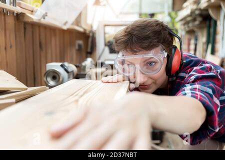 Junge attraktive 30-40 professionelle Tischlerin suchen Schleifen rohes Holz mit Schleifpapier in Schreinerei diy-Werkstatt. Weibliche Gleichberechtigung Stockfoto