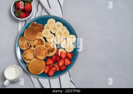 Trendiges Hausfrühstück mit Mini-Pfannkuchen und Erdbeere auf neutralem grauen Hintergrund. Über Ansicht mit Kopierbereich Stockfoto