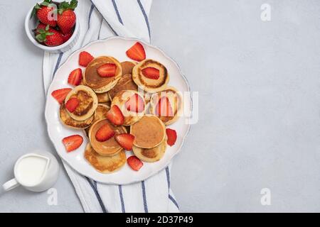 Blick von oben auf Mini-Pfannkuchen mit frischen Erdbeeren auf neutral Grauer Hintergrund mit Kopierbereich Stockfoto