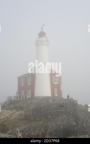 Eine einsame Figur geht am Fisgard Leuchtturm im herbstlichen Meeresnebel auf Vancouver Island, British Columbia, Kanada vorbei Stockfoto