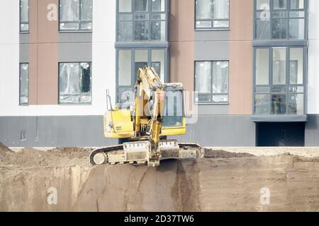 Bau eines Mehrfamilienhauses. Der Bagger führt die Arbeiten auf dem Planungsgebiet und der Vorbereitung des Fundamentgrabens durch. Im Hintergrund - Stockfoto