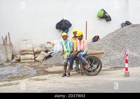 Antananarivo, Madagaskar - 24. April 2019: Gruppe unbekannter madagassischer Arbeiter in Schutzmützen und reflektierenden Jacken, die in der Nähe von Kieshaufen bei Bau stehen Stockfoto