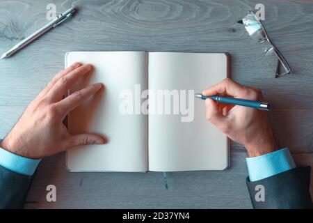 Hände von Geschäftsmann schriftlich in einem leeren Notizbuch mit Text Raum von oben betrachtet Stockfoto