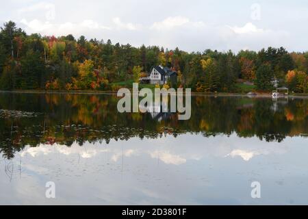 Eine Spiegelung der Häuser, Hütten und der Wald im French River im Herbst gesehen, in French River, Zentral-Ontario, Kanada. Stockfoto