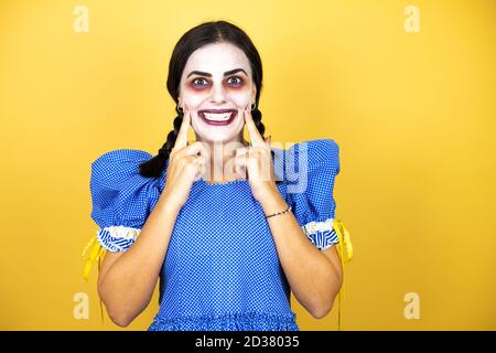 Frau trägt ein gruseliges Puppe halloween Kostüm auf gelbem Hintergrund Lächelnd selbstbewusst zeigen und zeigen mit den Fingern Zähne und Mund Stockfoto