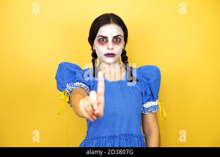 Frau trägt ein gruseliges Puppe halloween Kostüm auf gelbem Hintergrund Zeigt und zeigt mit den Fingern Nummer eins nach oben, während ist Ernst Stockfoto