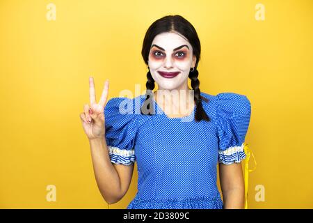 Frau trägt ein gruseliges Puppe halloween Kostüm auf gelbem Hintergrund Zeigen und zeigen mit den Fingern Nummer zwei beim Lächeln Selbstbewusst und glücklich Stockfoto