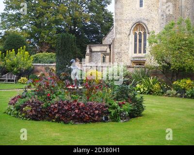 Chenies Manor Gärten im September mit St. Michael's Kirche. Statue des Amors in einem runden Blumenbett. Stockfoto