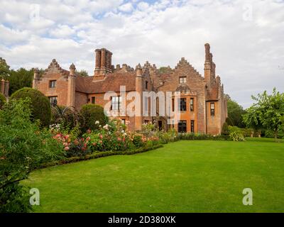 Chenies Manor House, ein Tudor Gebäude, und Garten im September mit. Dahlia Pflanzengrenze, Rasen, Maulbeerbaum gegen eine gesprenkelte Wolke gesetzt. Stockfoto
