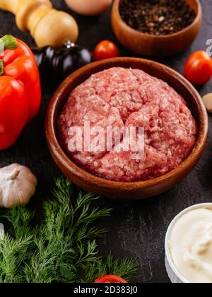 Frisches rohes Schweinefleisch in einer Holzschüssel mit Gemüse Im Hintergrund Stockfoto