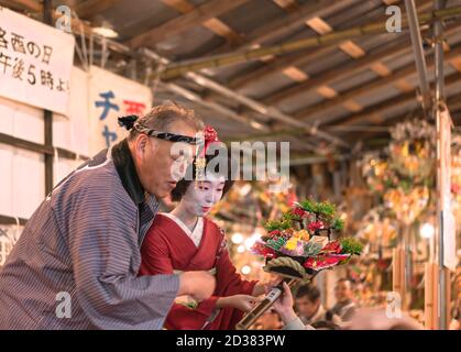 asakusa, japan - november 08 2019: Japanische Frau im Kimono hält einen glückverheißenden Rake oder kisshō Kumade mit einem Mann in Happi Jacke tun eine Lotterie an Stockfoto