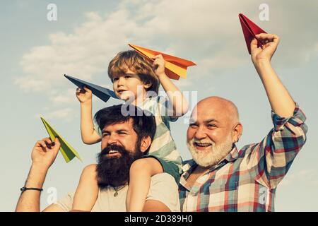 Glückliches Kind spielt im Freien. Glückliche Mann Familie viel Spaß zusammen. Kinder, die an sonnigen Tagen mit einfachen Papierflugzeugen spielen. Vater gibt Sohn fahren auf dem Rücken Stockfoto