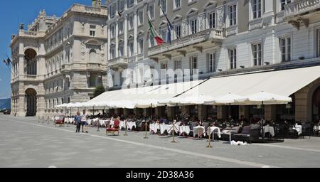 TRIESTE, ITALIEN - 20. Jun 2018: Piazza Unita d'Italia, Trieste, Italien, einschließlich Außentische eines Cafés unter einer Markise. Auch im Bild sind verschiedene pe Stockfoto