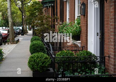 New York City, NY / USA - 7. Oktober 2020: Große graue, metallene Pflanzgefäße mit Laubpflanzen vor dem Ziegelsteinhaus in West Village, NYC Stockfoto