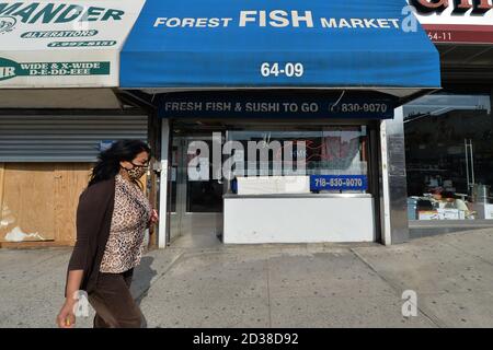 Eine Frau, die eine Maske trägt, geht an einem Fischmarkt vorbei, einem wichtigen Geschäft, in der Forest Hills Nachbarschaft von Queens, NY, 7. Oktober 2020. Gov. Andrew Cuomo hat ein dreistufiges Farbzonensystem (gelb, orange und rot) eingeführt, anstatt Postleitzahlen zu verwenden, um die Viertel zu identifizieren, die eine signifikante Spitze bei Coronavirus-Infektionen sehen, und verschiedene Einschränkungen auf der Grundlage der Farbe der Zone, rot ist die höchste. Die Beschränkungen der roten Zone umfassen maximal 10 Personen in Gotteshäusern, Gruppenversammlungen sind verboten, nur wichtige Unternehmen können offen bleiben, Schulen Stockfoto