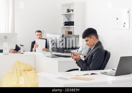 Porträt eines Mitarbeiters einer großen Organisation in der Kleiderordnung am Arbeitsplatz. Surfen im Internet auf einem Smartphone in sozialen Netzwerken. Stockfoto