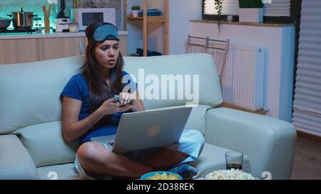Frau mit Schlaflosigkeit im Gespräch mit Mutter auf Webcam spät in der Nacht. Erschöpfte Person in Pijamas mit Schlafmaske mit Videoanruf auf Laptop-Computer sprechen mit Eltern mit Internet-Technologie. Stockfoto