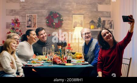 Teenager-Tochter nimmt ein Selfie mit der Familie bei weihnachten Reunion. Traditionelles festliches weihnachtsessen in einer Familie mit mehreren Generationen. Genießen Sie das Weihnachtsessen im dekorierten Zimmer. Großes Familientreffen Stockfoto