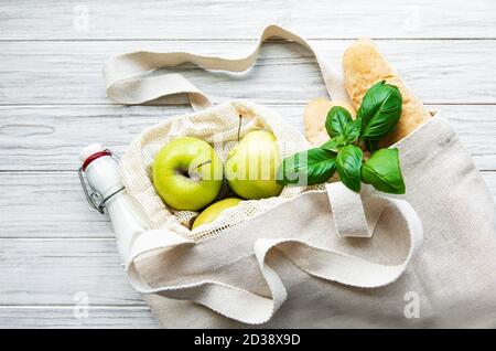 Frische Äpfel, Milch und Brot in Bio-Baumwollbeutel auf einem weißen Holztisch Stockfoto