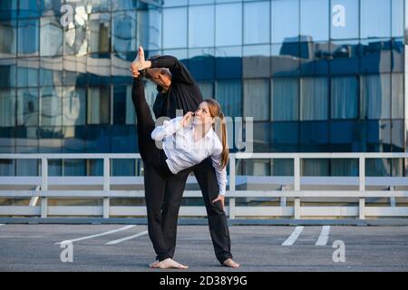 Flexible weibliche machen acro Yoga-Element, Stretching mit männlichen Basis Partner, während mit dem Handy sprechen im städtischen Hintergrund, Sport und Business Stockfoto