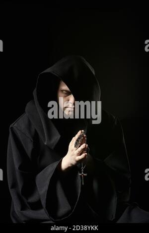 Assassin in dunkler Kleidung in der Kirche. Zauberer in schwarzem Mantel tun geheimnisvollen Ritus in dunklen Raum. Mönch betet in der Dunkelheit. Magisches Ritual im Schatten. Sinn Stockfoto