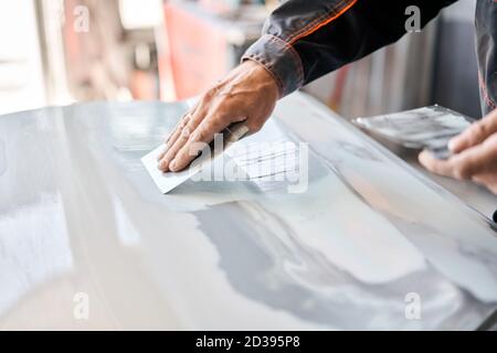 Reparatur Karosserie, Anwendung Kitt Nahaufnahme. Der Mechaniker repariert das Auto. Arbeiten Sie nach dem Unfall mit Schleifgrundierung vor dem Lackieren. Stockfoto