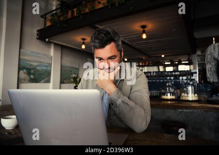 Gestresst männlich Blick auf Laptop neben einer Tasse Kaffee in einem düsteren Restaurant Stockfoto