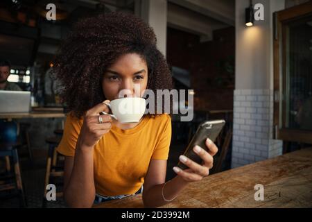 Junge und schöne afroamerikanische Frau schlürfen Kaffee in modischen Café. Stockfoto