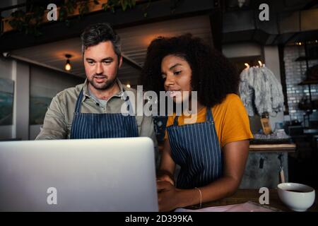Kellner und Kellnerin lernen neue Speisekarte vom Laptop und trinken heiß Kaffee steht im trendigen Cafe Stockfoto