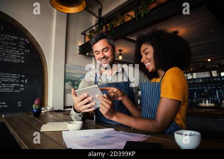 Manager und Kellnerin lachen über Designs auf digitalen Tablet stehen Mit heißem Kaffee im Café Stockfoto