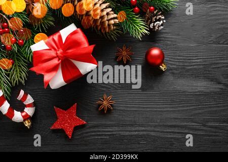 Weihnachts-Geschenkbox mit roter Schleife und Verzierungen auf schwarz Holzhintergrund