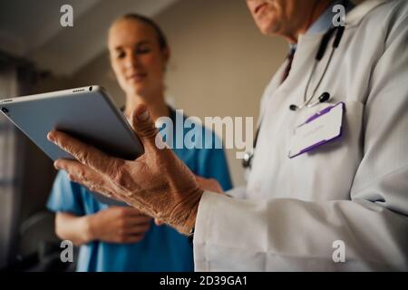 Nahaufnahme von männlichen Arzt hält digitale Tablette, während weiblich Praktikant hört Anweisungen stehen in organisierten Büro Stockfoto