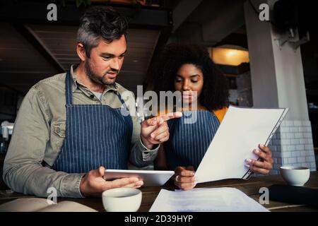 Männliche und ethnische weibliche Kaffeehaus Besitzer diskutieren Geschäft in Coffee Shop. Stockfoto