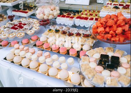 Nahaufnahme der Hochzeitssockbar mit verschiedenfarbigen hellen Cupcakes, Makronen, Kuchen, Gelee und Obst. Süßes Urlaubsbuffet mit Süßigkeiten und anderen d Stockfoto