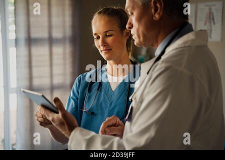 Männlicher Arzt diskutiert Patienten Ergebnisse auf digitale Tablette mit weiblich Krankenschwester in Scrubs Stockfoto