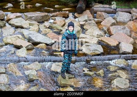 Glückliches Kind, Junge im Wald auf Felsen in der Nähe Teich, spielen im Regen, Herbsttag Stockfoto