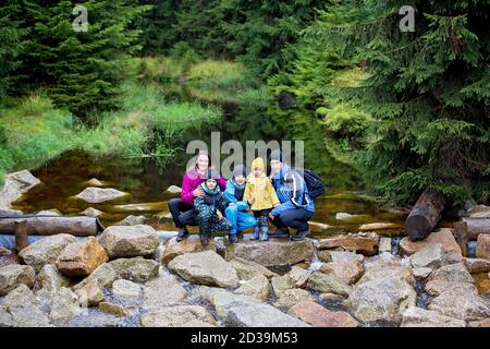 Glückliche Menschen, Kinder mit Eltern im Wald auf Felsen in der Nähe Teich, spielen im Regen, Herbsttag Stockfoto