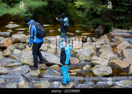 Glückliche Menschen, Kinder mit Eltern im Wald auf Felsen in der Nähe Teich, spielen im Regen, Herbsttag Stockfoto