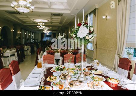 In den elegant eingerichteten Sälen des Restaurants werden Banketttische für die Gäste serviert. Hochzeitsdetails. Blumenarrangements auf den Tischen. Foto-Spalte Stockfoto