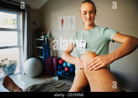 Konzentrierte weibliche Physiotherapeutin Biegen Knie des männlichen Patienten auf Massageliege im Pilates Zimmer liegend. Stockfoto