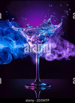 martini Cocktail spritzt auf rauchblauem und purpurem Hintergrund Stockfoto