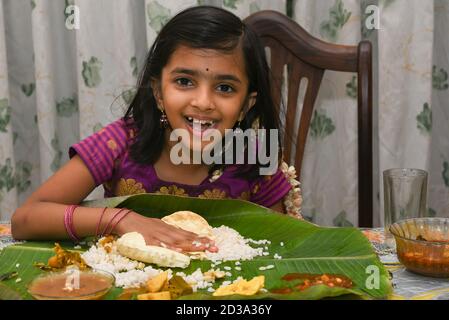 Kerala Onam Festival, glücklich indisches Mädchen Kind Essen Onam sadhya mit Hand tragen traditionelle Kleidung, Indien. Lächelndes junges asiatisches Kind. Schönes Kind Stockfoto