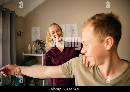 Weibliche Physiotherapeutin Stretching Arm der kaukasischen Patientin. Stockfoto