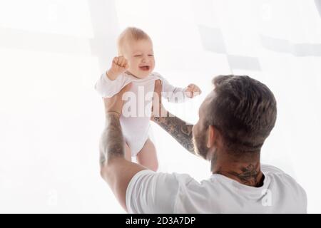 Rückansicht des jungen Vaters, der aufgeregt Junge in hält Ausgestreckte Hände Stockfoto