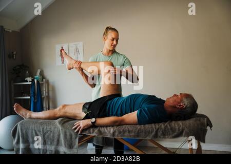Physiotherapeutin führt eine Knieanalyse für ältere Männer durch Stockfoto